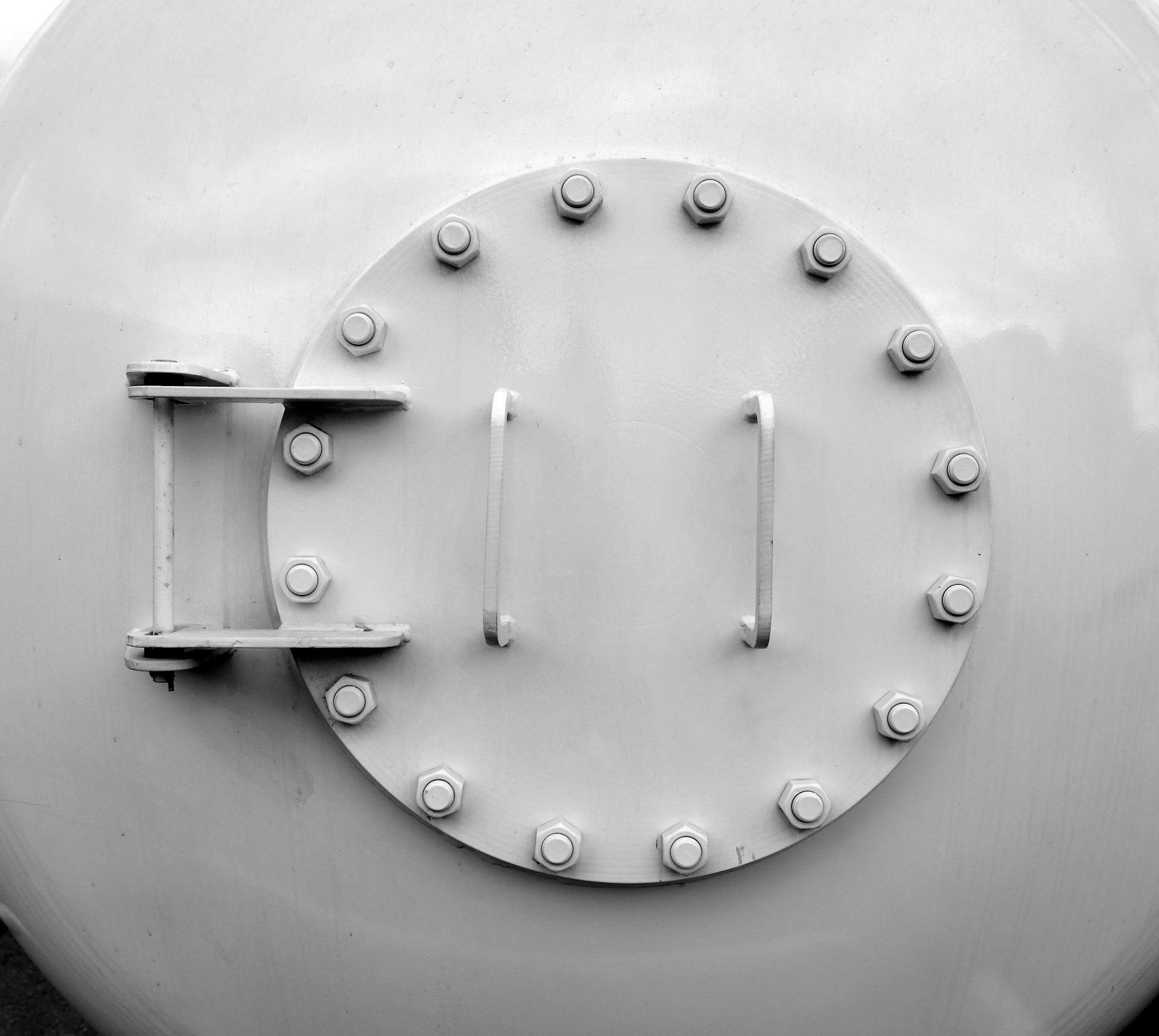 A grey image of a heavy metallic round door with large secure screws and bolts for safety