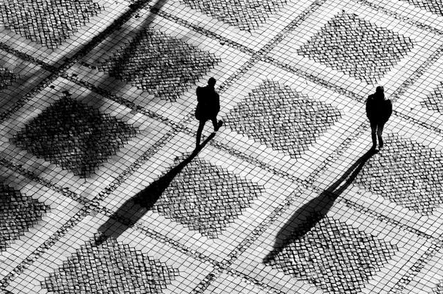 Aerial view of people and shadows outdoors on a tiled square.
