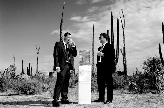 two men in suits standing in desert drinking water