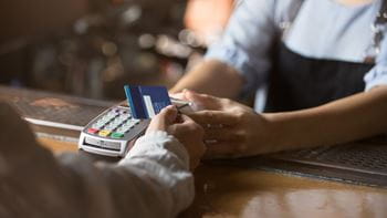 person's hand holding a credit or debit card to a card reading machine which is being help by a person wearing black apron