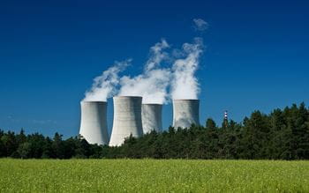 nuclear power plant steaming against a blue sky and green grass in the foreground