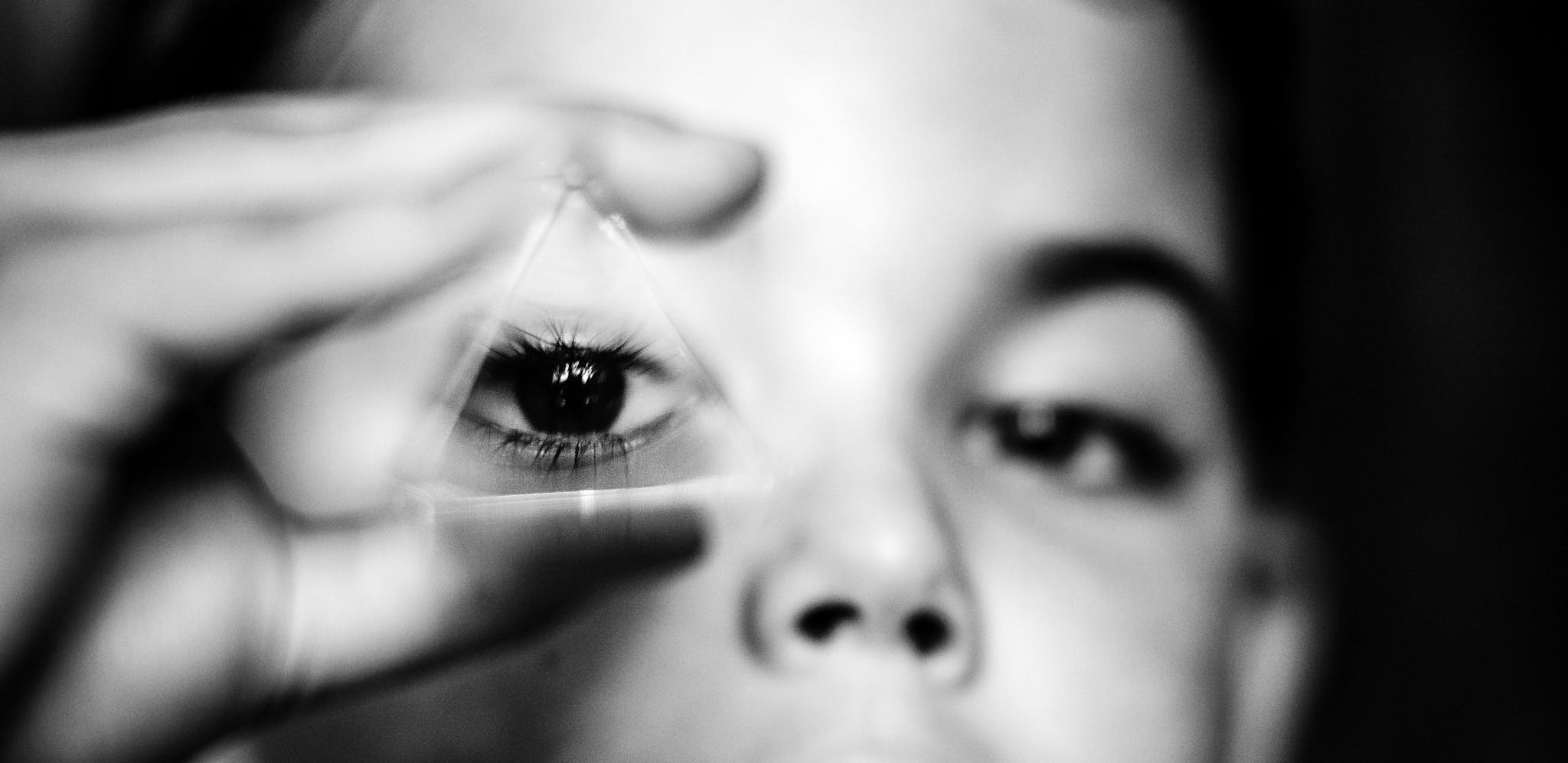 Black and white image of a child looking through a glass triangular object which magnifies his eye
