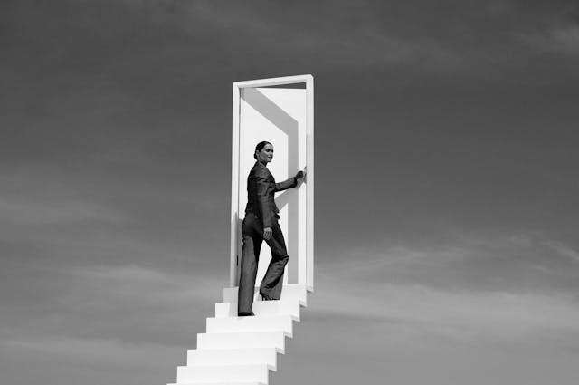 A person reaching the top of stairs and opening a door in the clouds