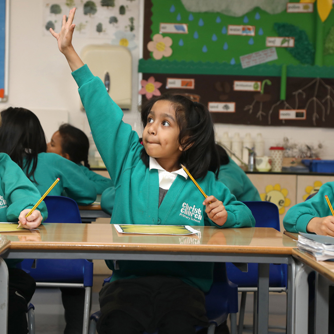 A young student in the classroom raising her hand to answer a question