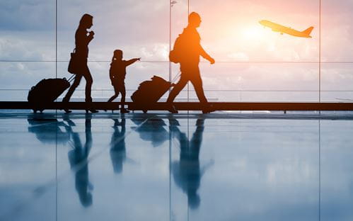 two adults and a child wheeling their luggage through an airport with a plane taking off in the background