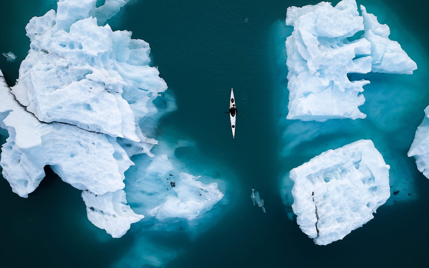 Aerial shot - several ice bergs in blue water with small canoe floating in the middle