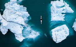 Aerial shot - several ice bergs in blue water with small canoe floating in the middle