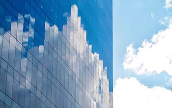 office high tower with glass front mirroring blue sky and white clouds 
