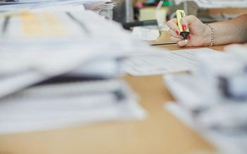documents at a desk and a person highlighting text with a yellow marker
