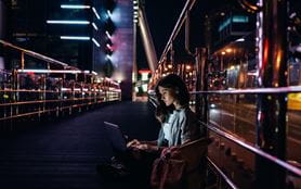 Image of a person sitting on a bridge using a laptop