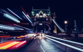 City light trails of red bus in traffic on Tower Bridge in London at night