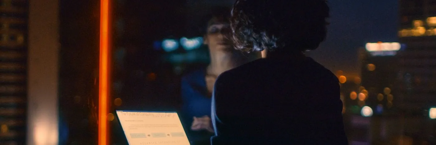 Woman looking through window at night holding laptop