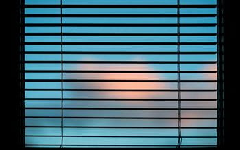 Blue sky with pink clouds seen through window with silhouette of venetian blinds