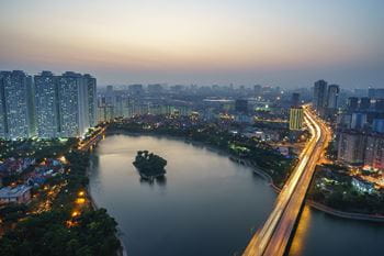City at sunset with a large body of water and motorway leading into the distance with vehicle light trails