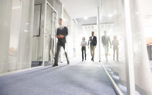 Two men and a woman are walking down an office corridor