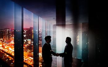 Two people shaking hands in office next to window showing city skyline
