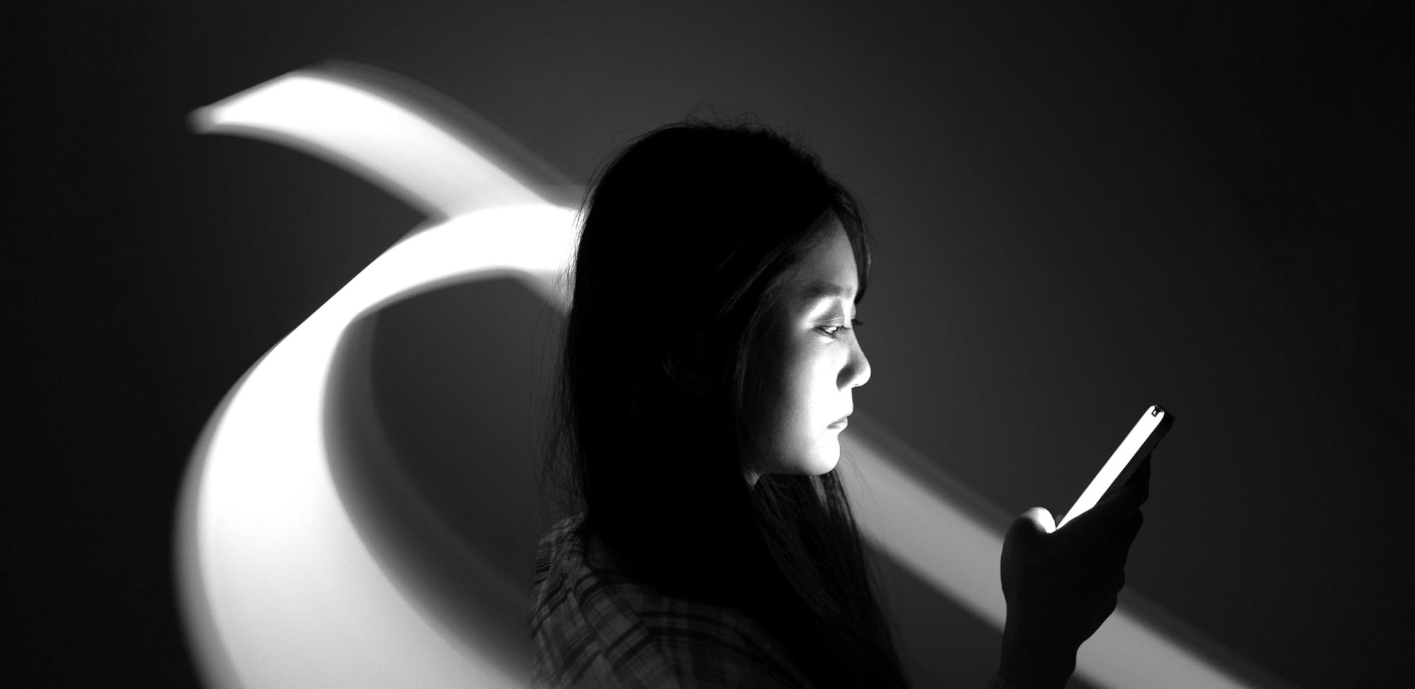 A person uses a mobile phone while two beams of light curve around them