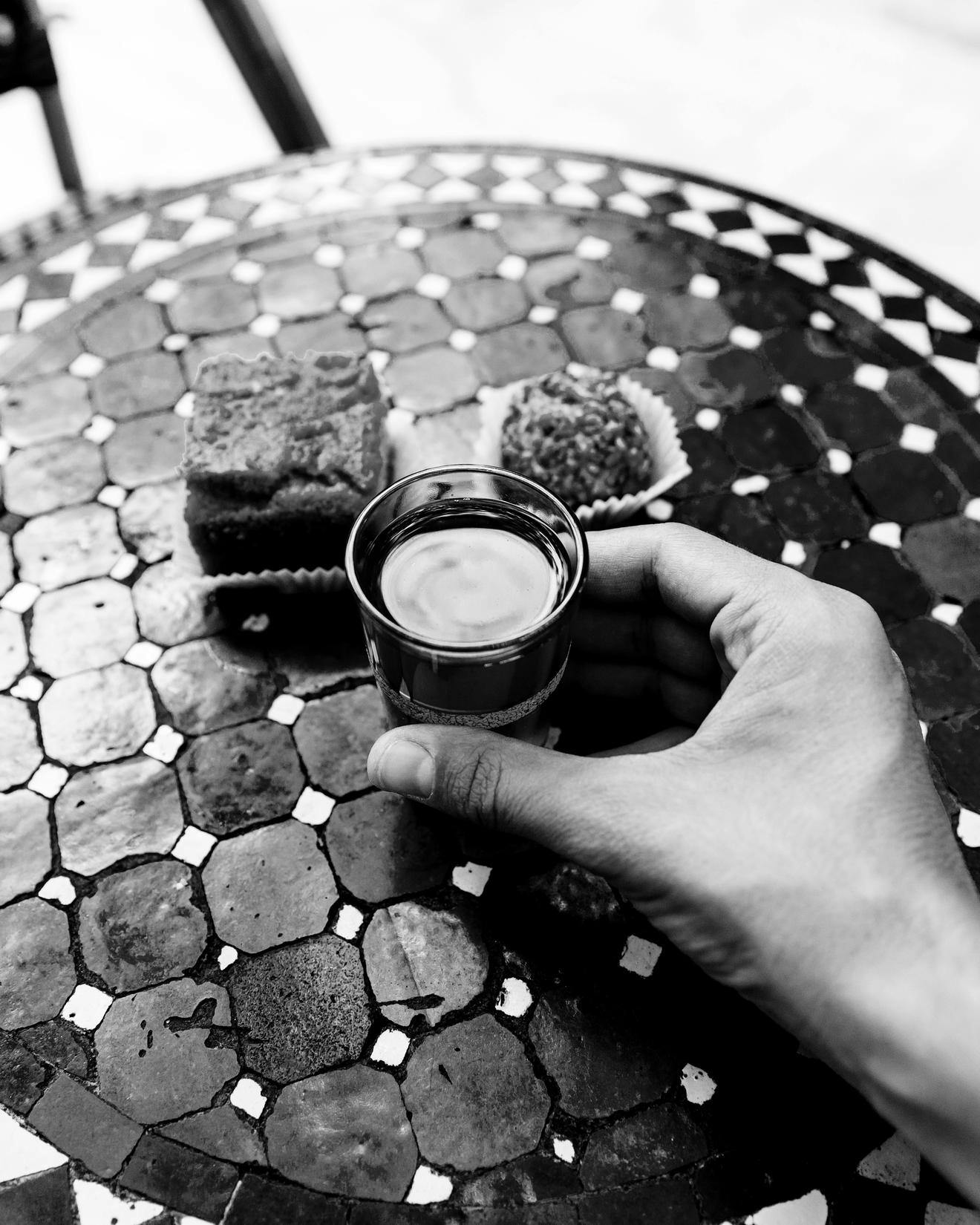 Black and white image of someone sitting at a tiled table for tea and cakes in Morocco