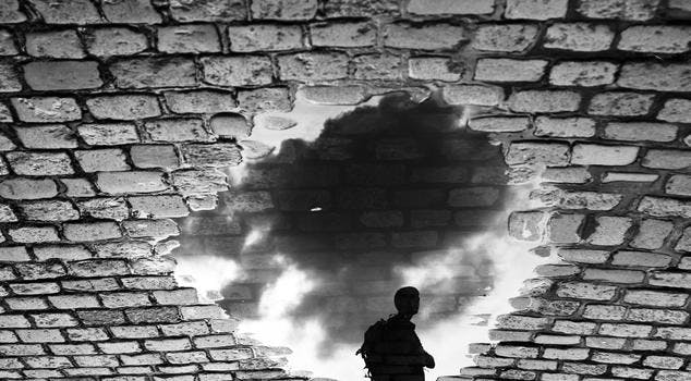 Man standing in front of a hole in brick wall with a cloudy sky behind him
