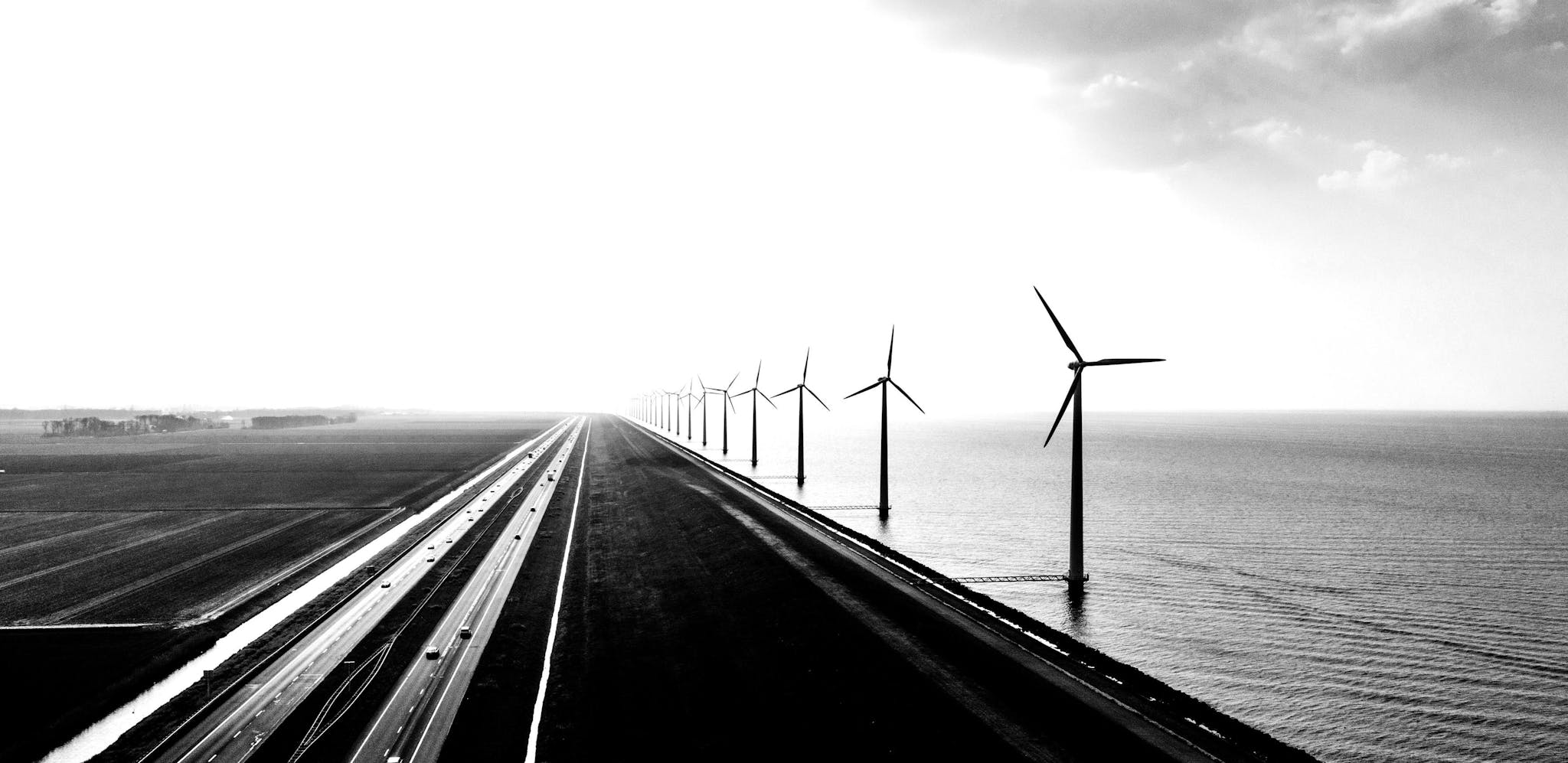 A waterside road in Europe with wind turbines running along side